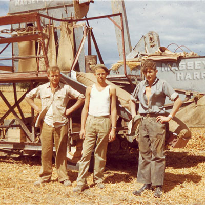 Old photo of father and sons. Peter and sons by old harvester in field.